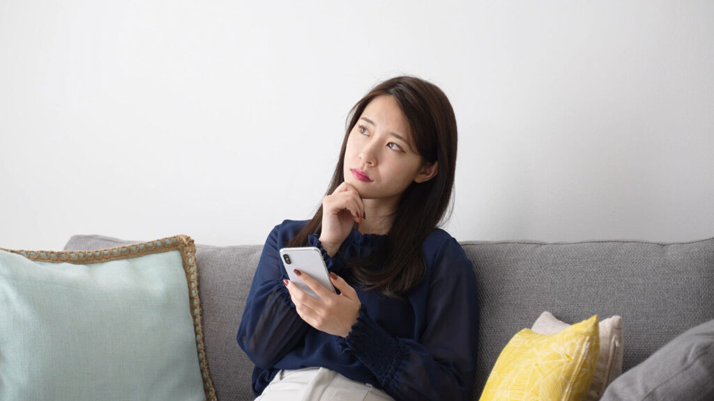スマホを手に考え込む女性(チャットレディに向いてるか悩んでいるイメージ)