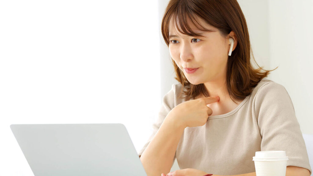 パソコンの前で自分を指さしながら話す女性(話す力と聞く意識があるイメージ)