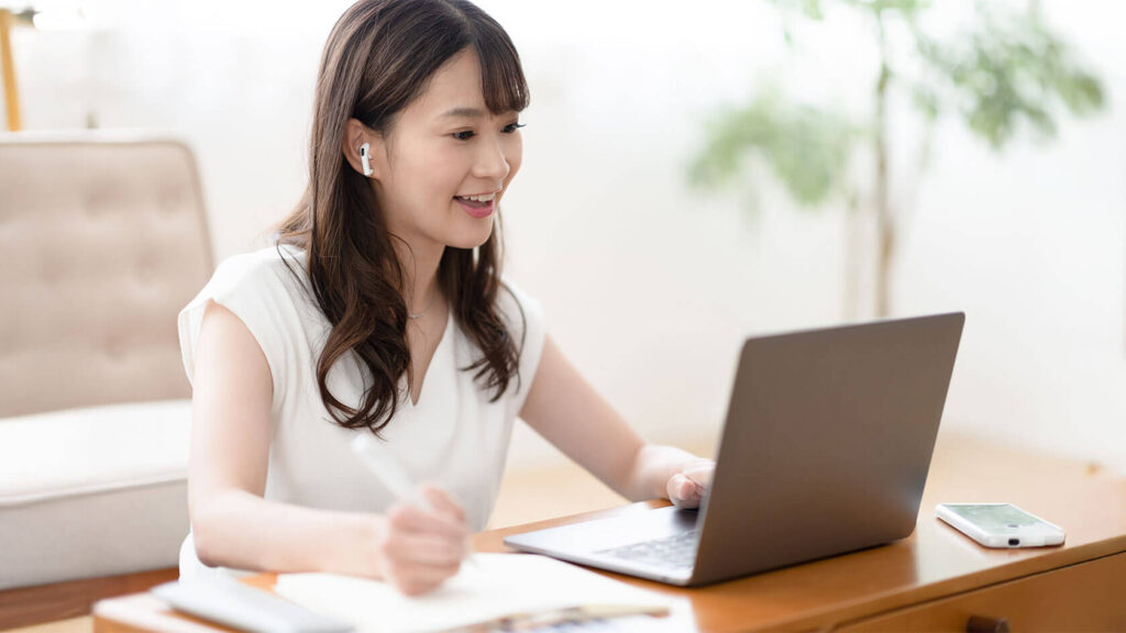 アルバイトのシフト表と教科書、ノートパソコンを並べて学業とチャットレディを両立する女子学生